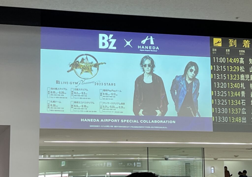 羽田空港第1ターミナル1階のフライトインフォメーションサイネージにB'zの広告が表示される様子